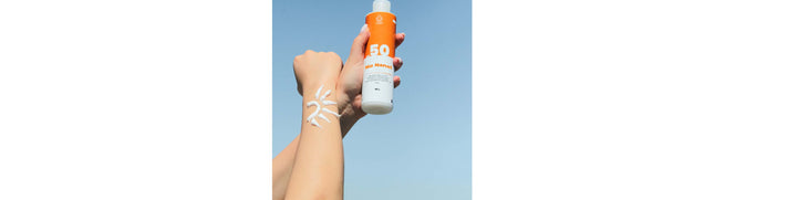 "Hand holding a sunscreen bottle with SPF 50 label, while sunscreen is applied in the shape of a sun on the forearm against a clear blue sky