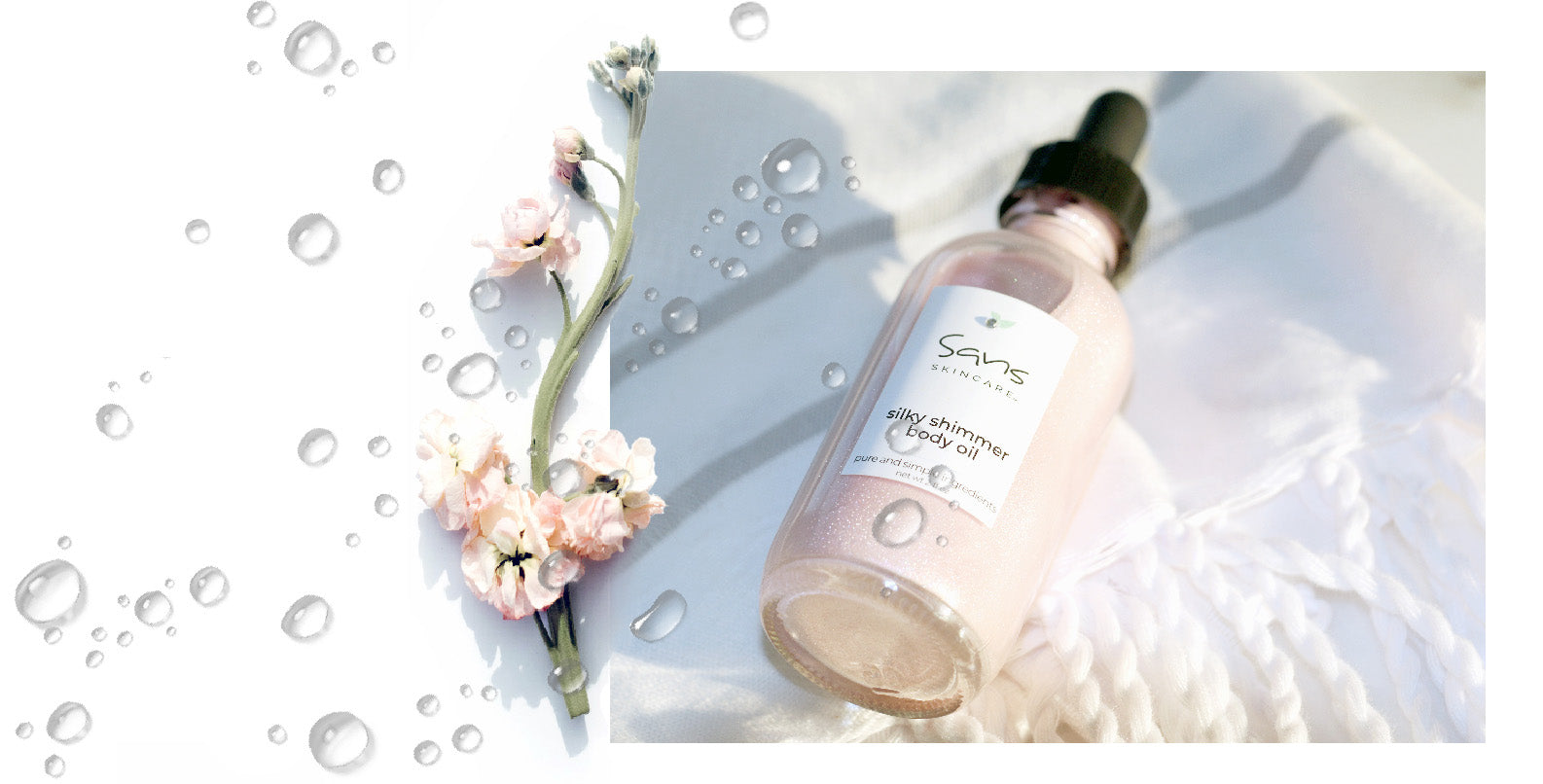 Sans Skincare Silky Shimmer Body Oil in glass dropper bottle with pink flowers and water droplets on white fabric background