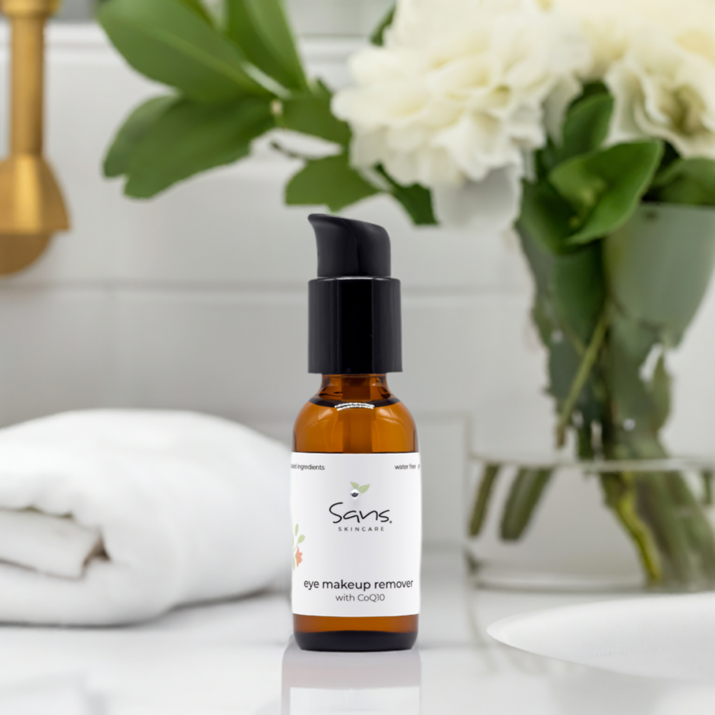 Sans Skincare Eye Makeup Remover with CoQ10 in amber pump bottle on bathroom counter with white towel and flowers