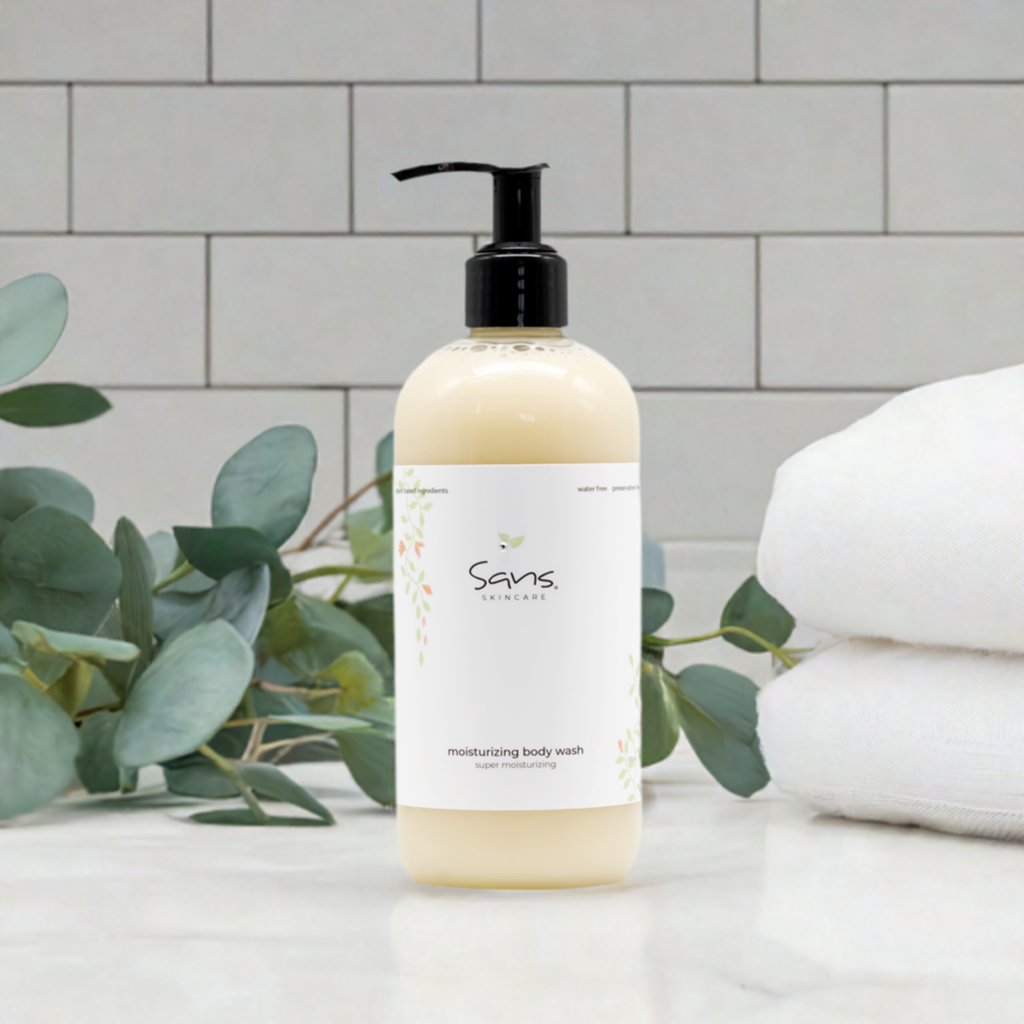 Sans Skincare Moisturizing Body Wash in cream-colored pump bottle displayed on a bathroom counter with eucalyptus leaves and folded white towels in the background